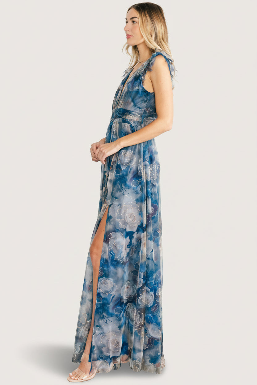 Studio shot of the Adelyn Maxi Dress in blue floral displayed full-length to show overall silhouette, banded waist, and slit placement.