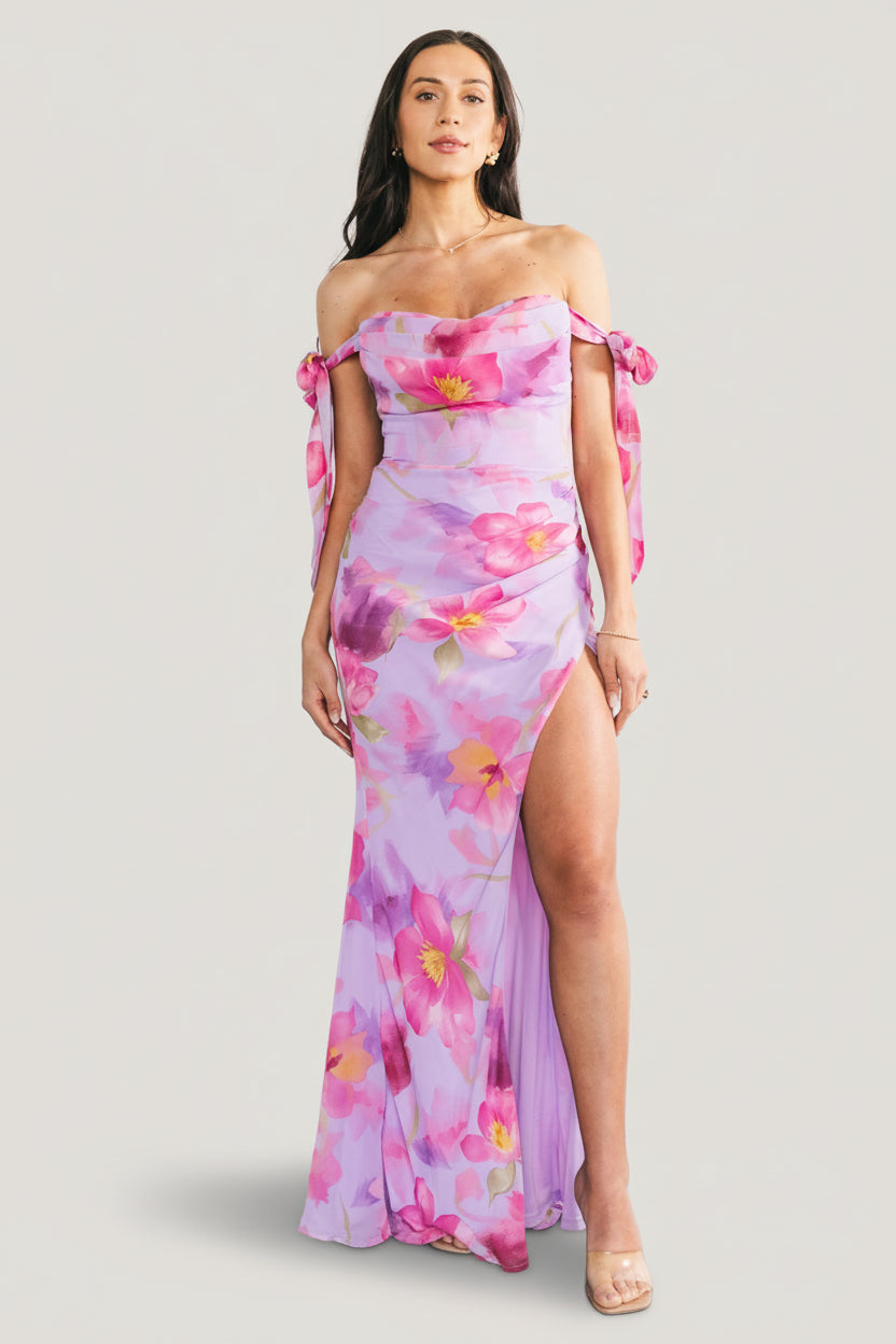 Full-length front view of lavender floral chiffon maxi dress on model, showing off-shoulder bow straps and flowing tulip skirt.