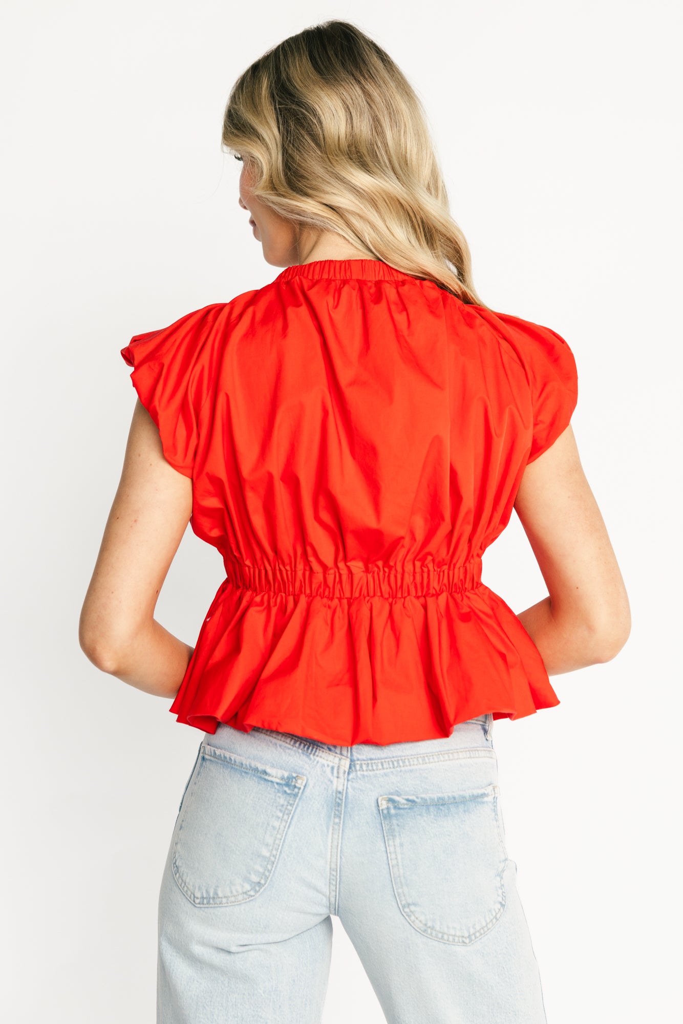 Back view of the coral Norma ruffle peplum top on a model showing clean lined back and the gently flared peplum hem.