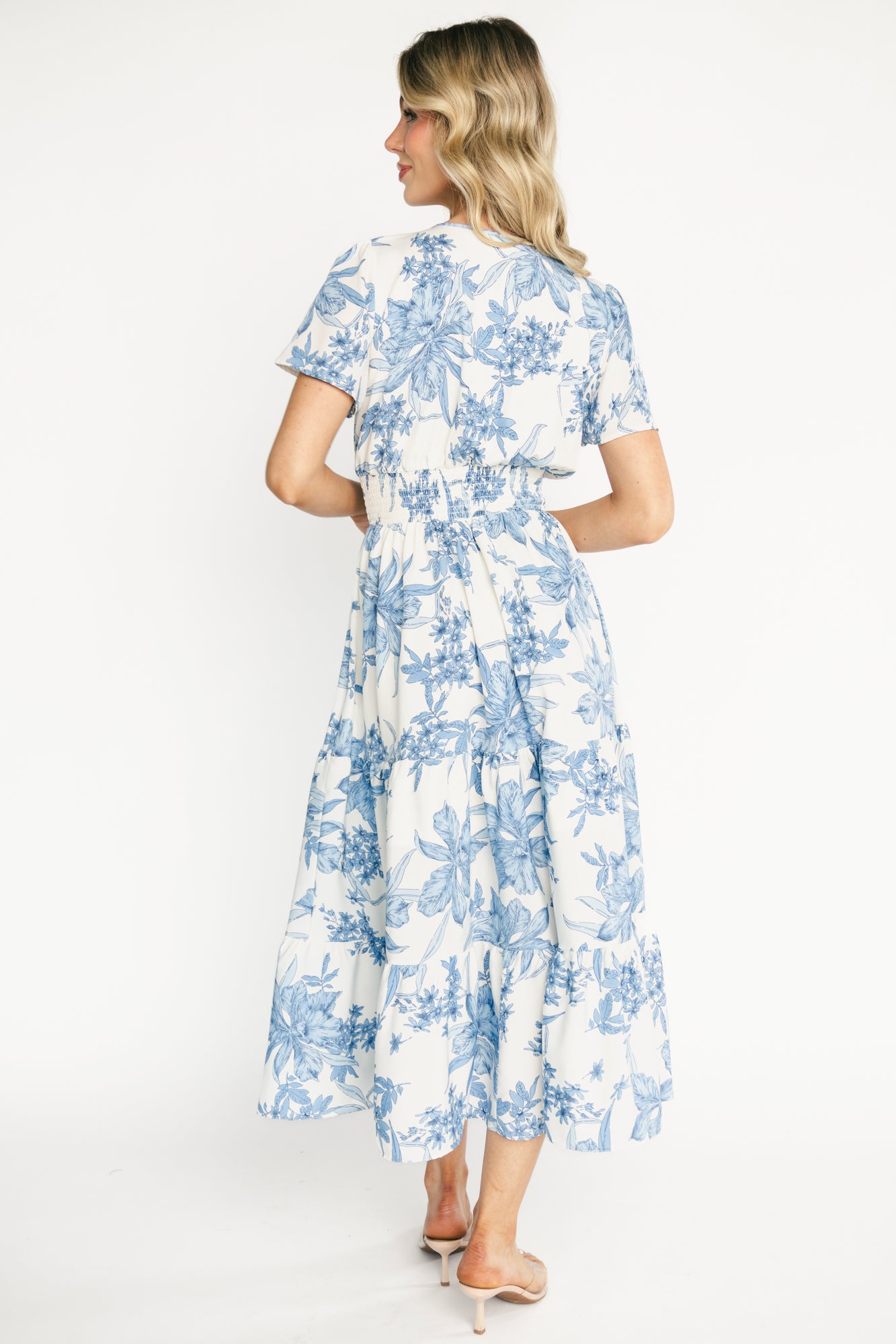 Back view of the Holland midi dress on a model, showing the flutter short sleeves, V-neckline, and overall silhouette in blue floral print.