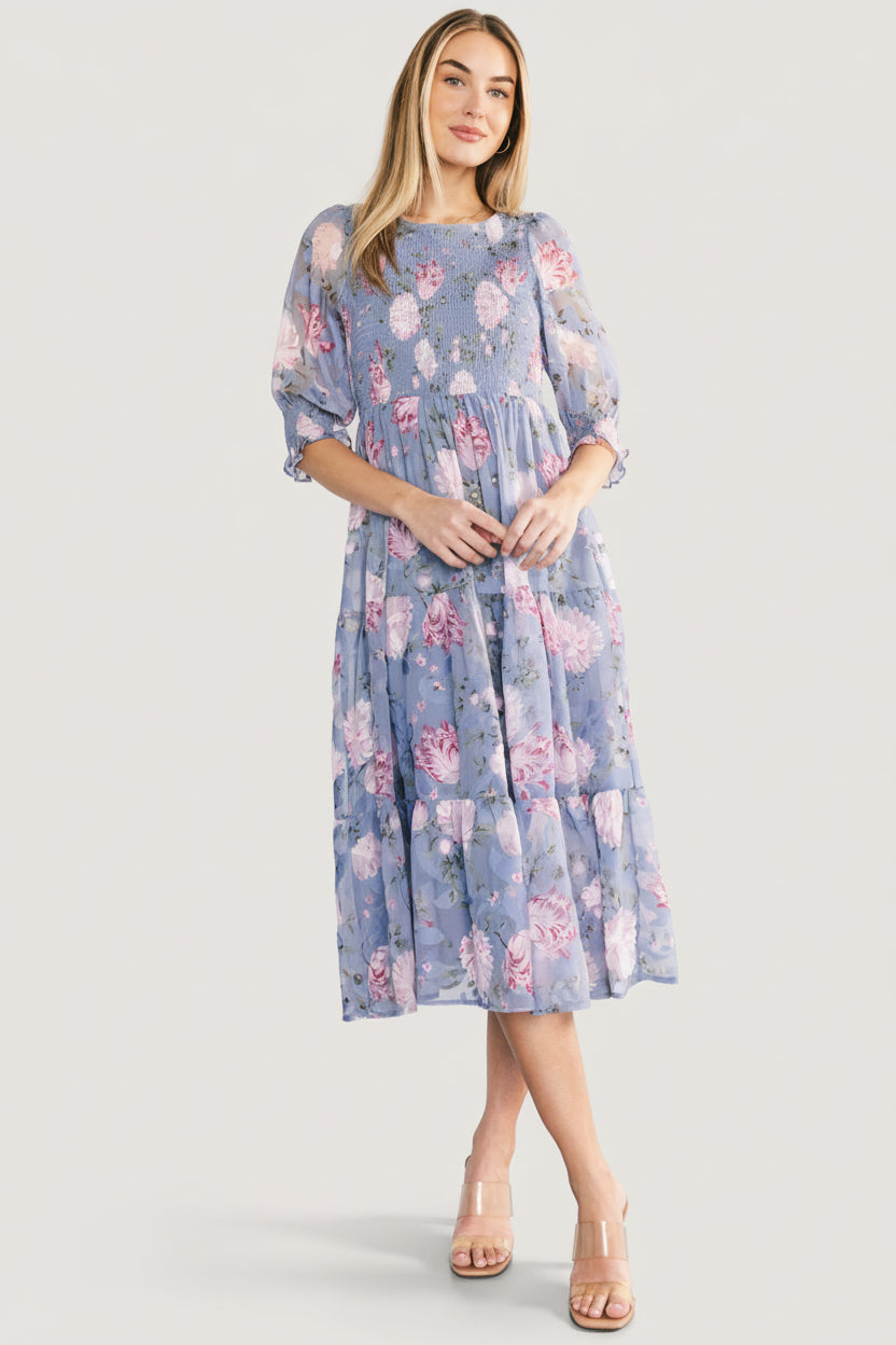 Three-quarter angle of dusty blue floral Nellie dress highlighting smocked bodice and delicate burnout botanical print across fabric.