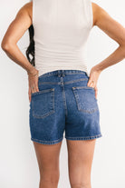 Close-up of the zipper and button closure on medium-wash denim, showing textured fabric and the frayed hem detail of the Lennon shorts.