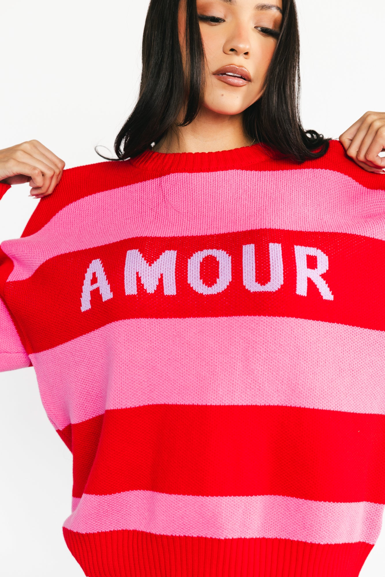 Three-quarter view highlighting the sweater’s oversized silhouette, ribbed hem, and the playful alternating pink and red stripe design.