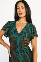 Three-quarter side view showing empire waist and flowing skirt of the Kimberly velvet maxi dress in jade and bronze floral velvet.