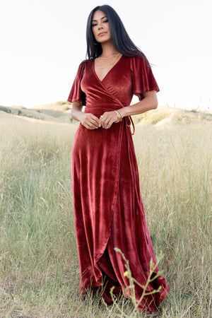 Front view of model wearing terracotta velvet Katelyn maxi wrap dress with higher-coverage V-neck, medium flutter sleeves, and tulip skirt.