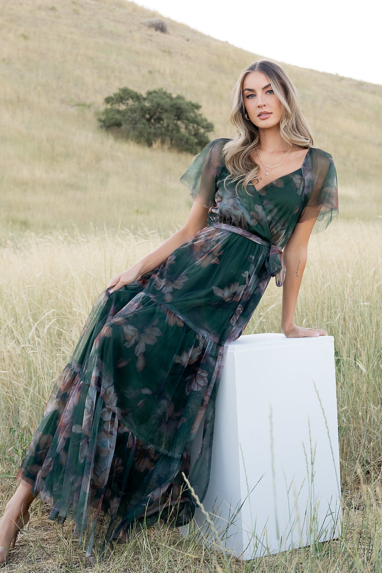 Side view of Nicola dress in deep green floral, showing removable self-tie at waist and soft drape of layered tulle over lining.