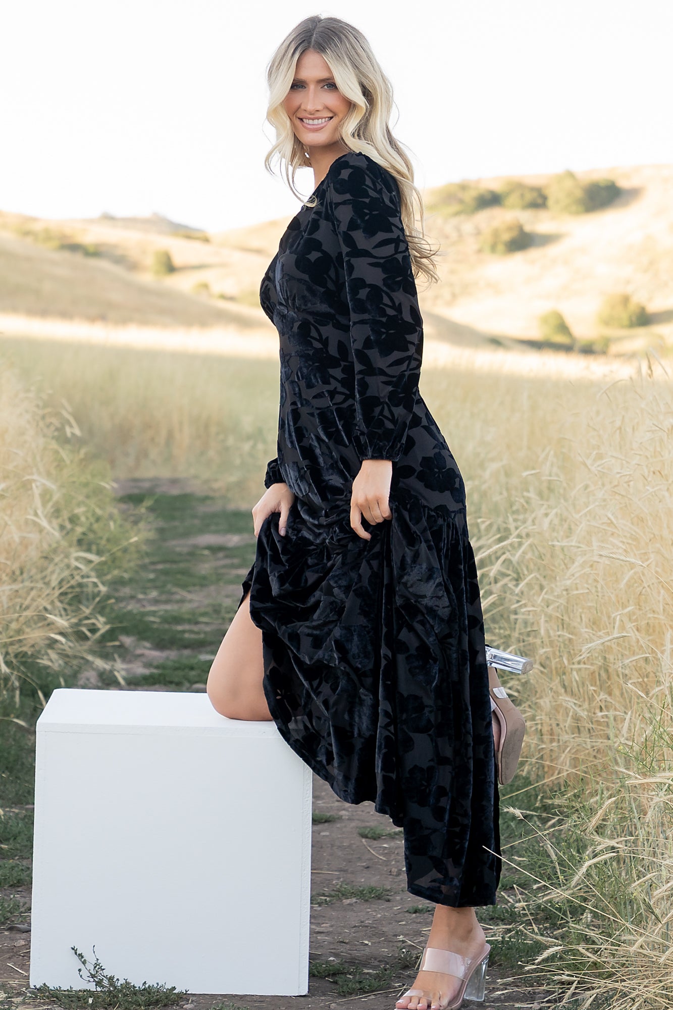 Full outfit shot on model walking to showcase the dress's tiered maxi skirt movement, long sleeves, and overall evening-ready silhouette.