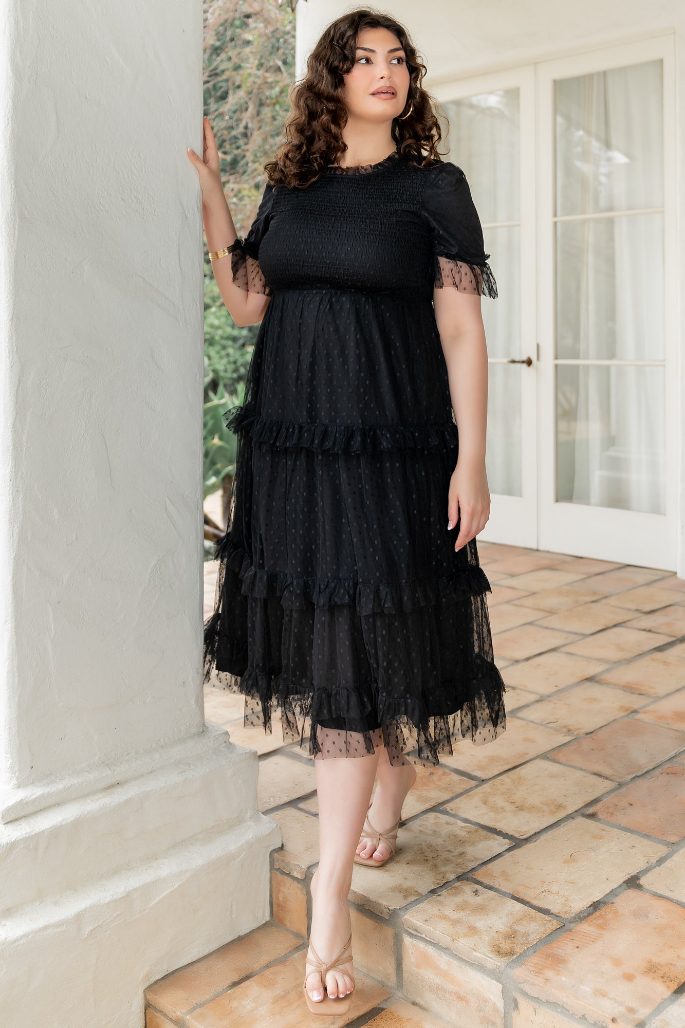 Side and movement shot of the Lysandra Smocked Dot Maxi Dress in black showing tiered midi skirt, ruffle cuffs, and soft tulle texture while twirling.