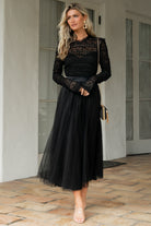 Full-length front view of the Lonnie Tulle Dress in black on a model, showing lace bodice, ruffled overlay, satin waist tie, and flowing tulle midi skirt.