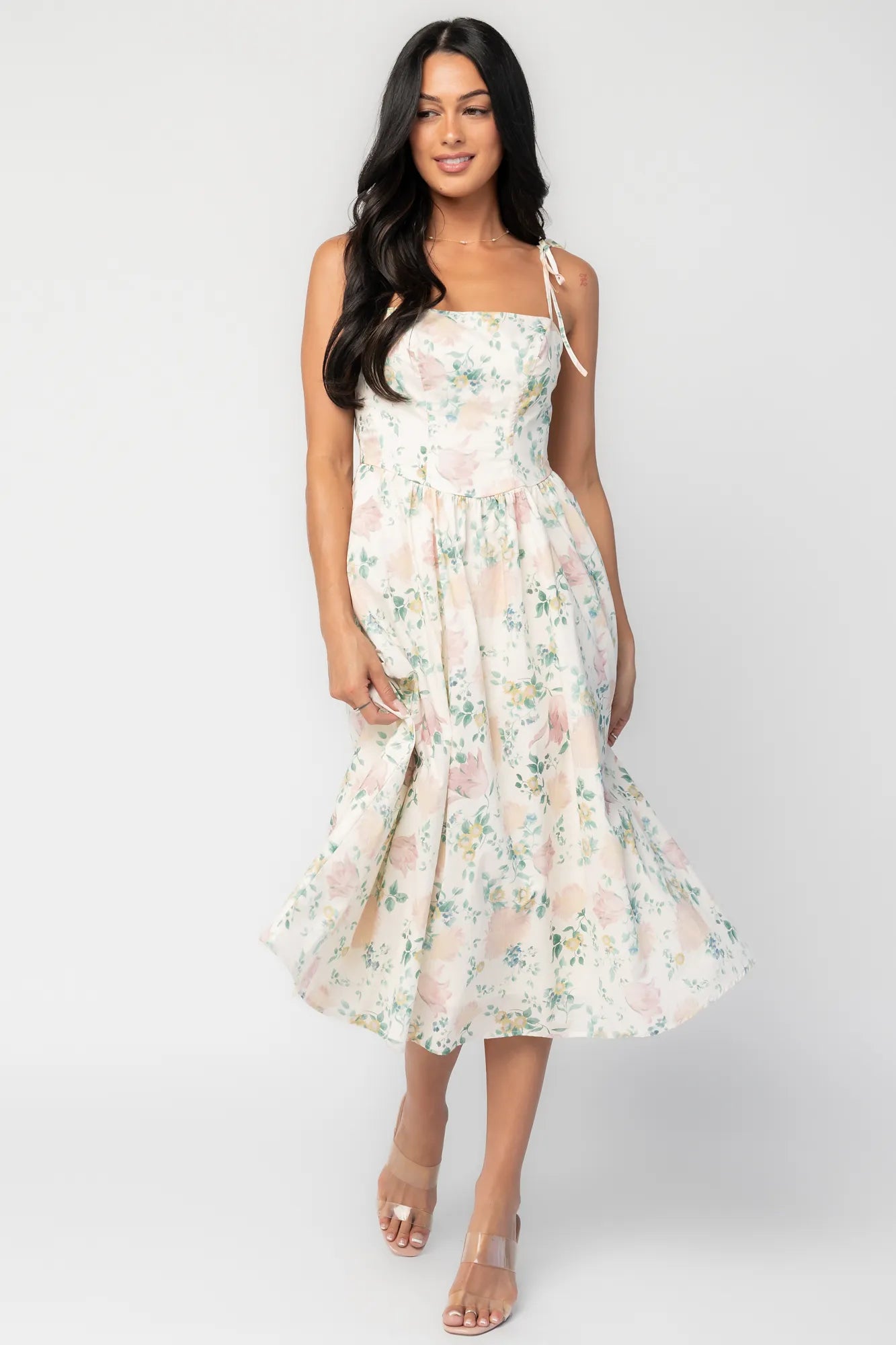 Model wearing a cream floral midi dress with a square neckline, adjustable shoulder tie straps, fitted bodice, and flowing skirt. 