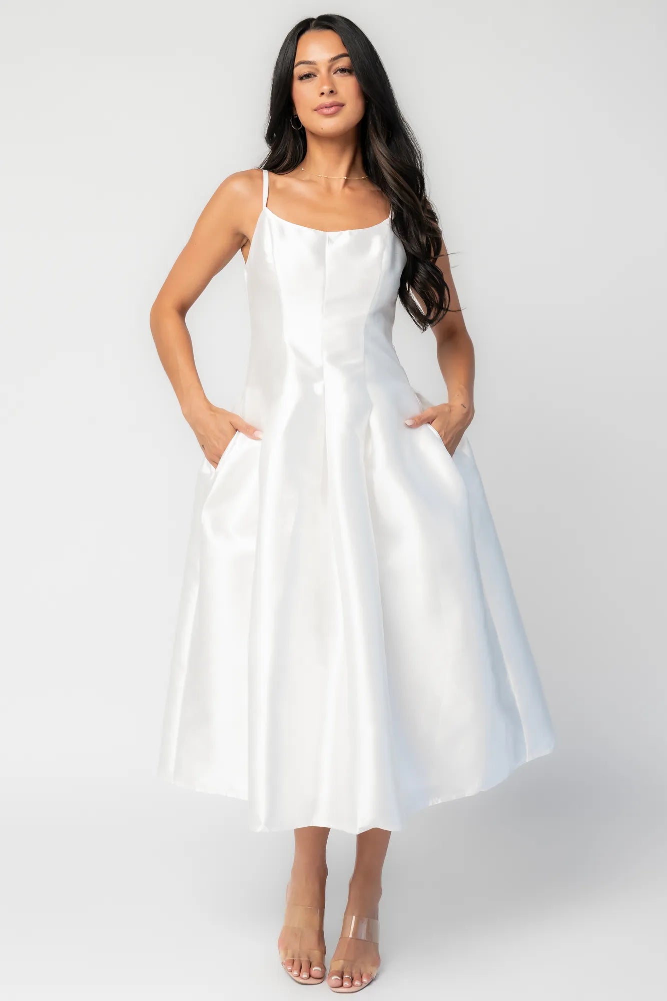 Woman wearing a white sleeveless midi dress with a fitted bodice, side pockets, and a full A-line skirt.