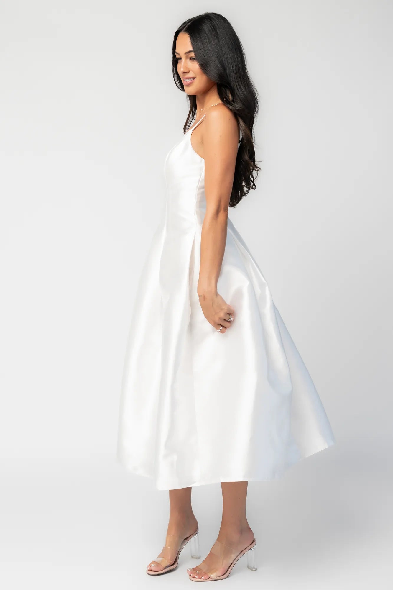 Woman wearing a white sleeveless midi dress with a fitted bodice, side pockets, and a full A-line skirt.