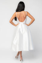 Woman wearing a white sleeveless midi dress with a fitted bodice, side pockets, and a full A-line skirt.