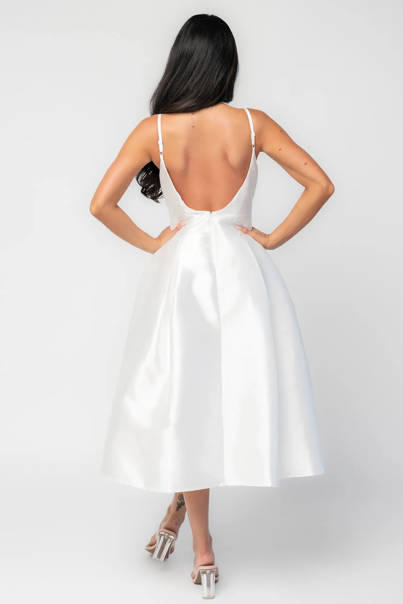 Woman wearing a white sleeveless midi dress with a fitted bodice, side pockets, and a full A-line skirt.