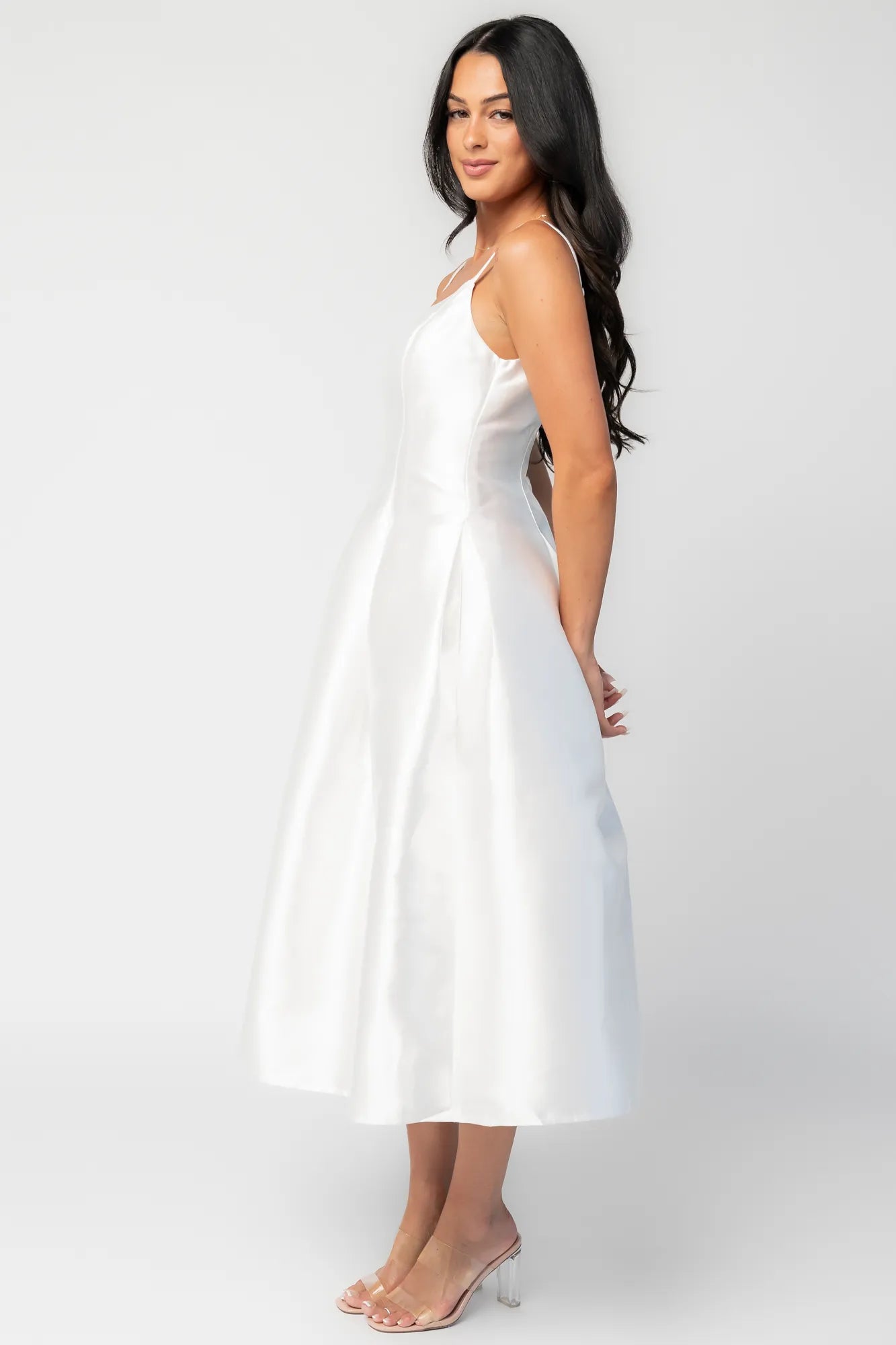 Woman wearing a white sleeveless midi dress with a fitted bodice, side pockets, and a full A-line skirt.