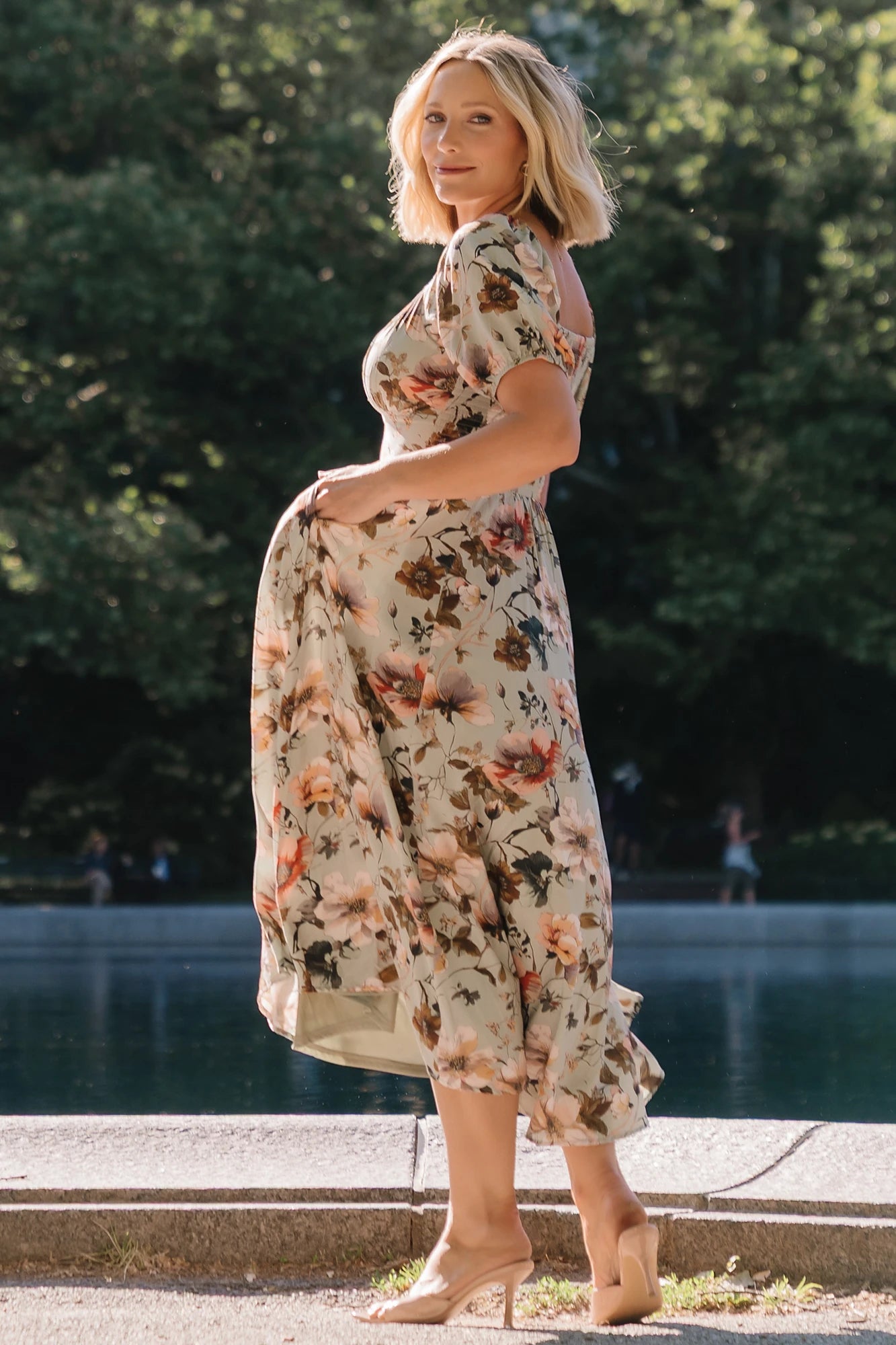 Model wearing the Charlotte Midi Dress in Sage, a sage green midi dress with a pink multi floral print, rounded square neckline, puff sleeves, banded waist, and flowing A-line skirt with side pockets.