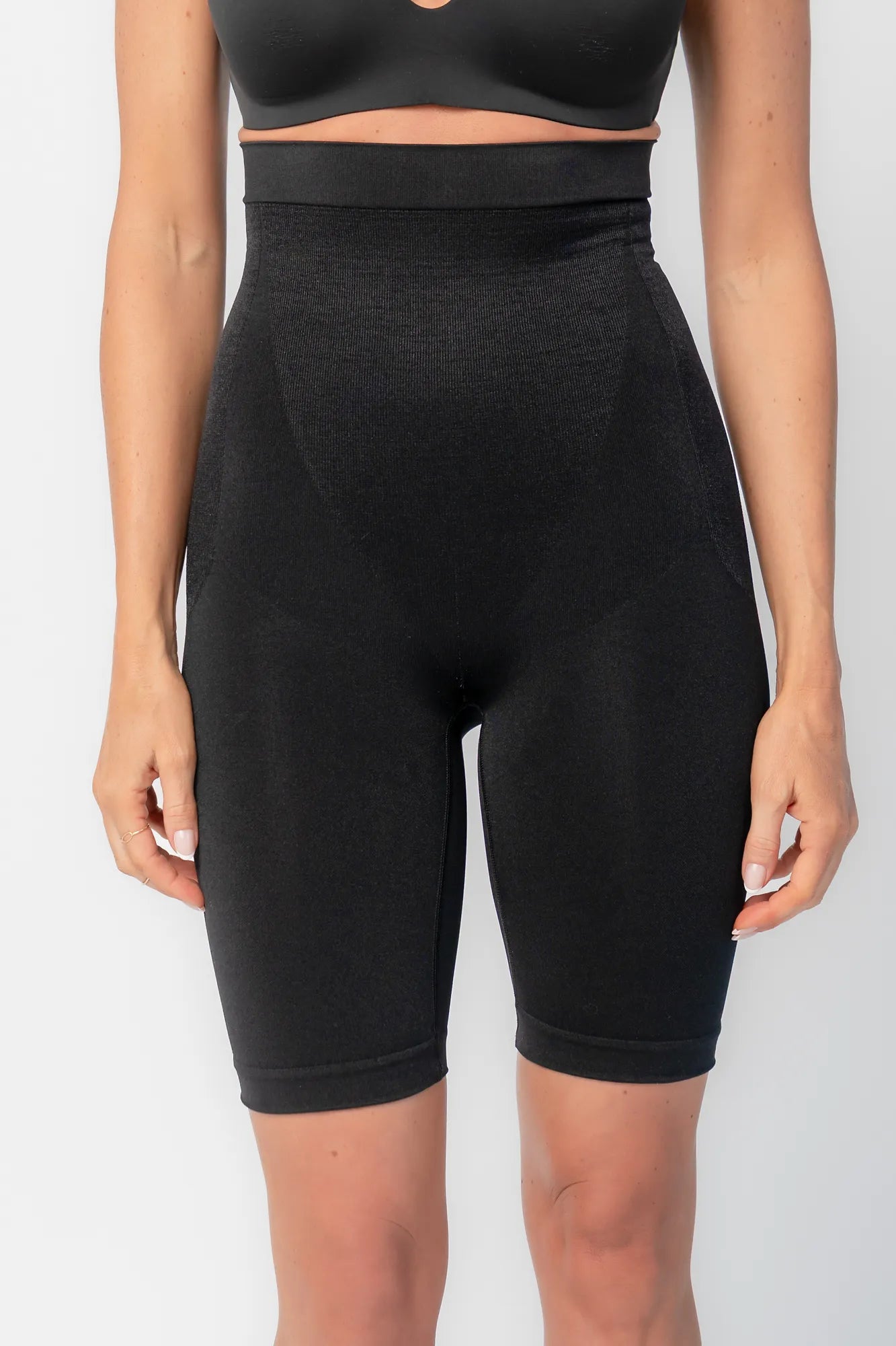 Model wearing black high-waisted shaping shorts with a seamless design and mid-thigh length.