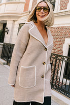 Taupe collared knit cardigan with cream contrast trim, a button-front closure, long sleeves, and two front patch pockets in a relaxed, shirt-style silhouette.