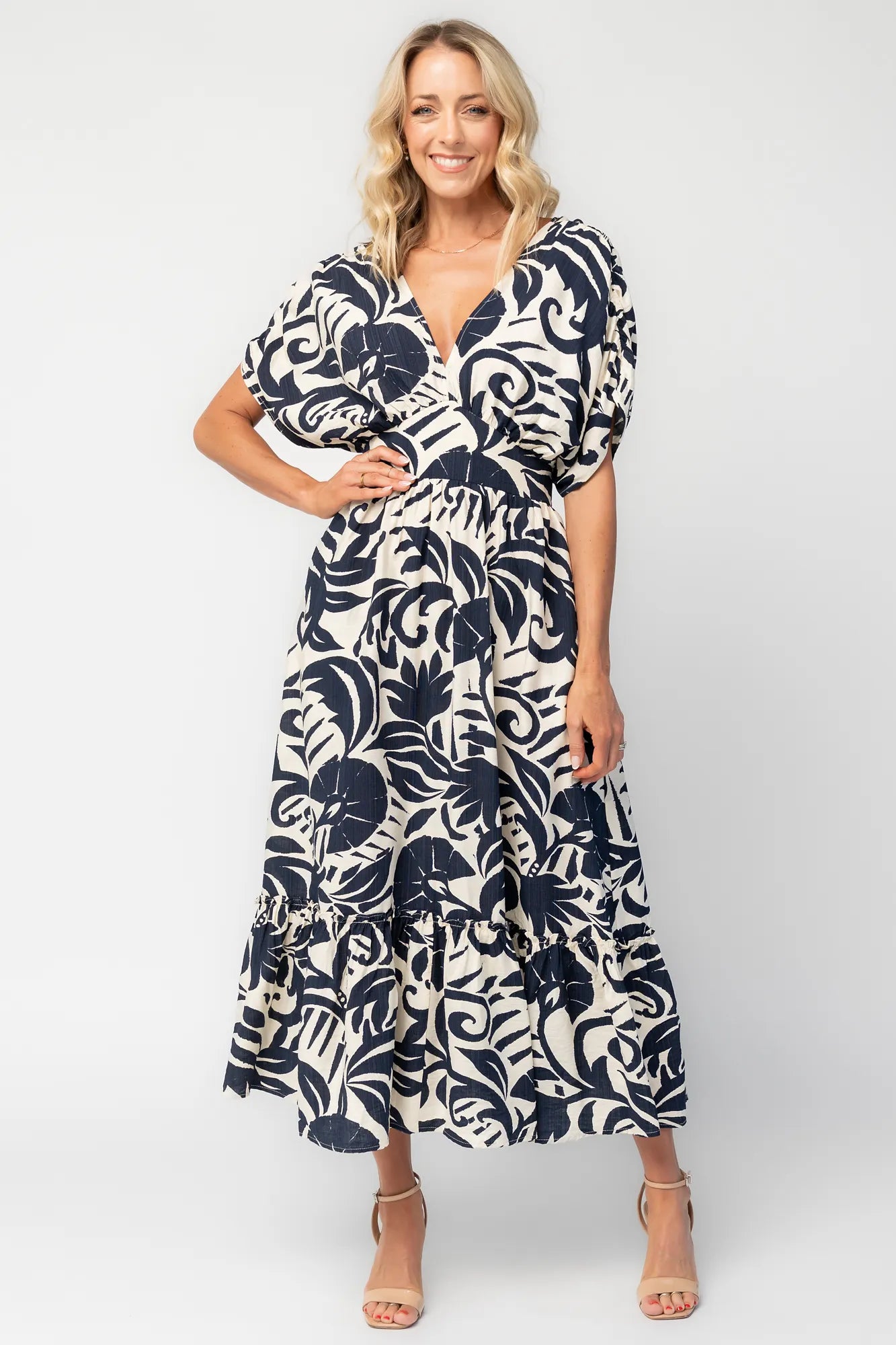 Woman wearing a navy and ivory printed midi dress with a V-neckline, short sleeves, an empire waist, and a tiered hem.