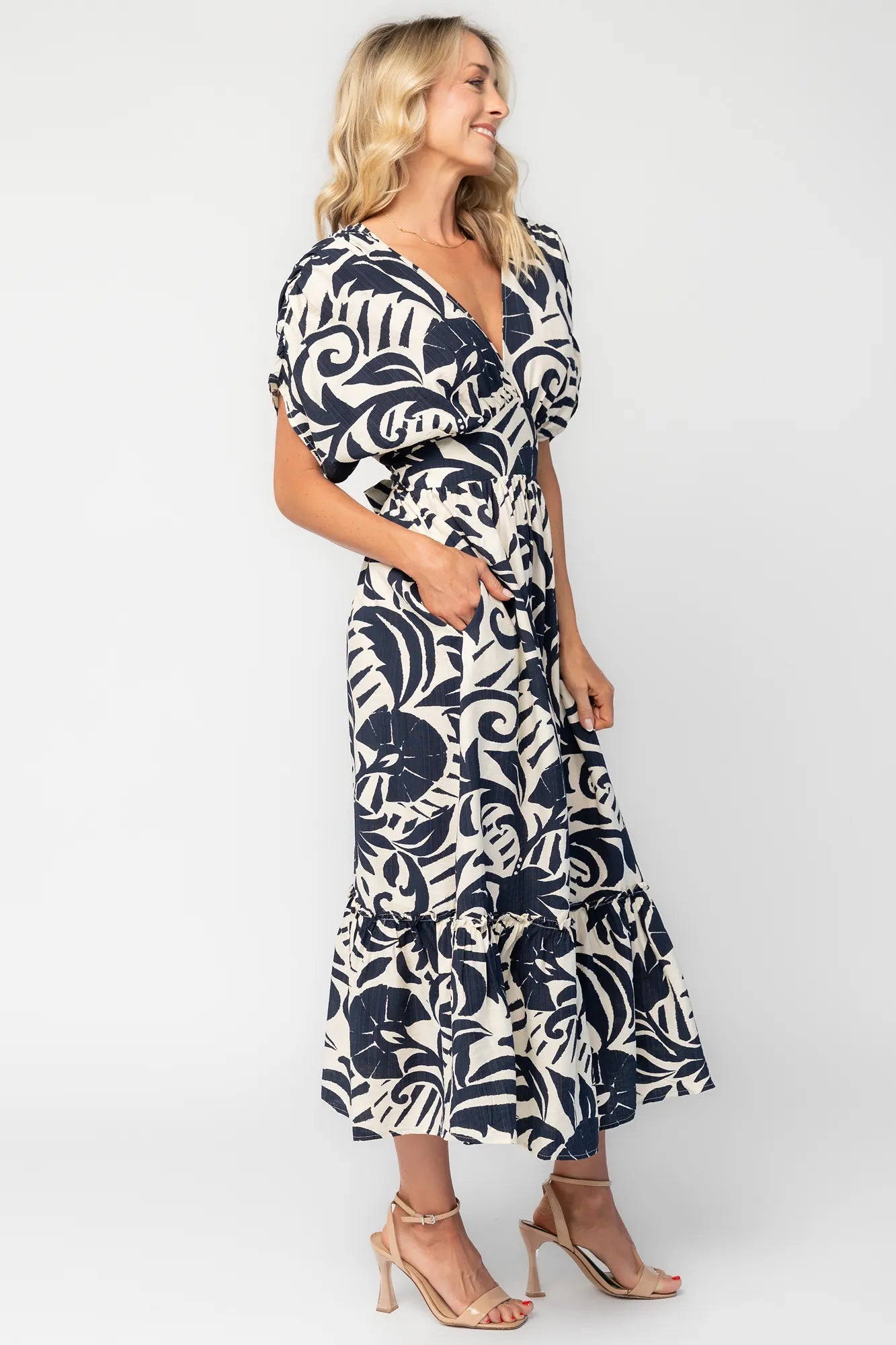 Woman wearing a navy and ivory printed midi dress with a V-neckline, short sleeves, an empire waist, and a tiered hem.