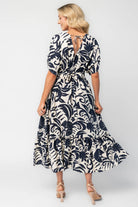Woman wearing a navy and ivory printed midi dress with a V-neckline, short sleeves, an empire waist, and a tiered hem.