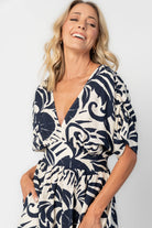 Woman wearing a navy and ivory printed midi dress with a V-neckline, short sleeves, an empire waist, and a tiered hem.