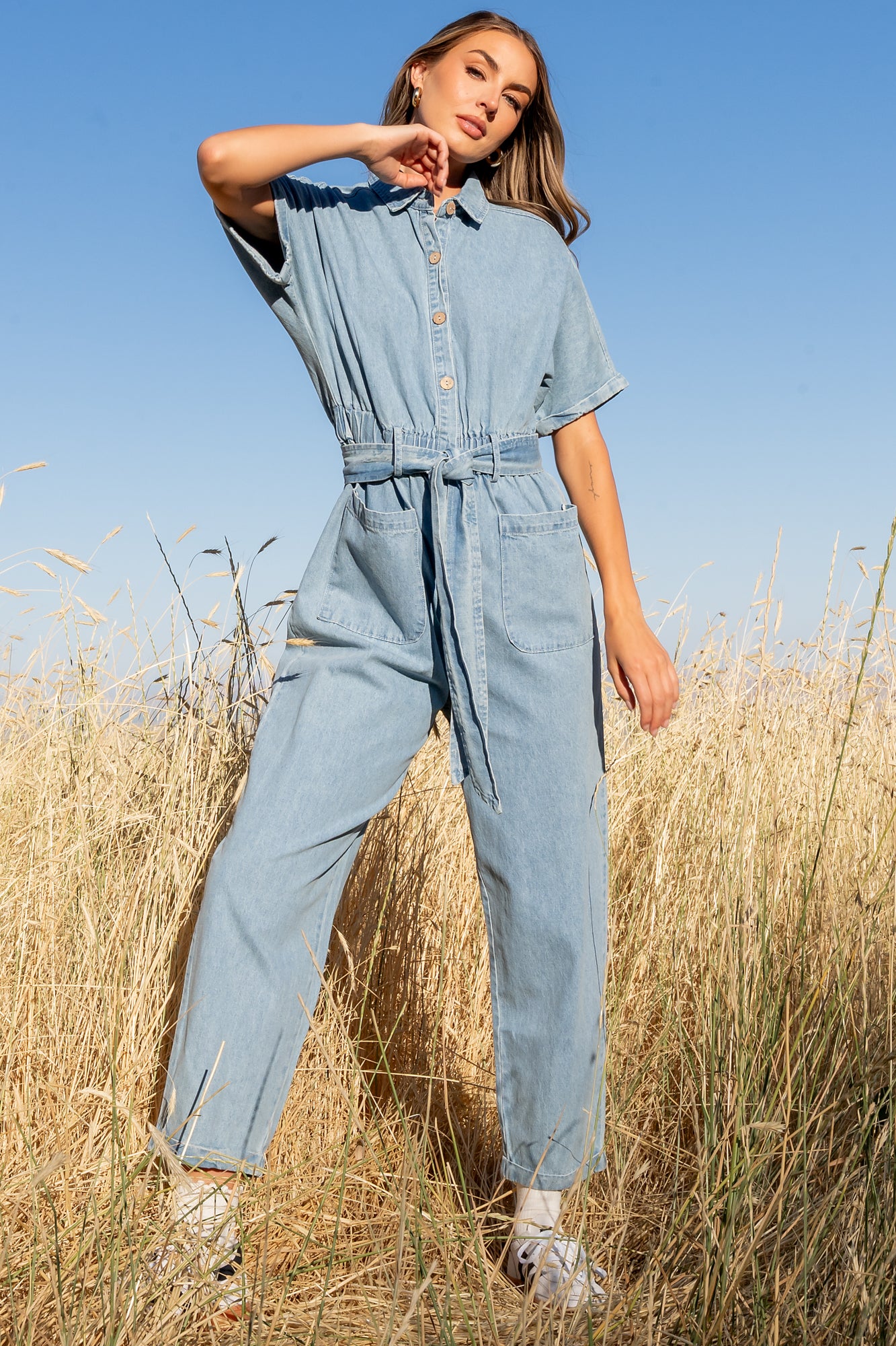 Front view of Mateo washed denim jumpsuit on model with shirt collar, elastic waist, and cropped tapered legs.