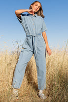 Front view of Mateo washed denim jumpsuit on model with shirt collar, elastic waist, and cropped tapered legs.