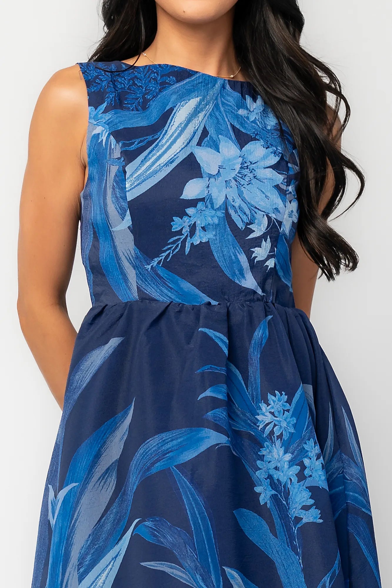 Model wearing a navy sleeveless midi dress with a high boat neckline and a fitted bodice. 
