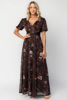 Model wearing a clove floral maxi dress with a deep V-neckline, short sleeves, and an empire waist.
