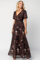 Model wearing a clove floral maxi dress with a deep V-neckline, short sleeves, and an empire waist.