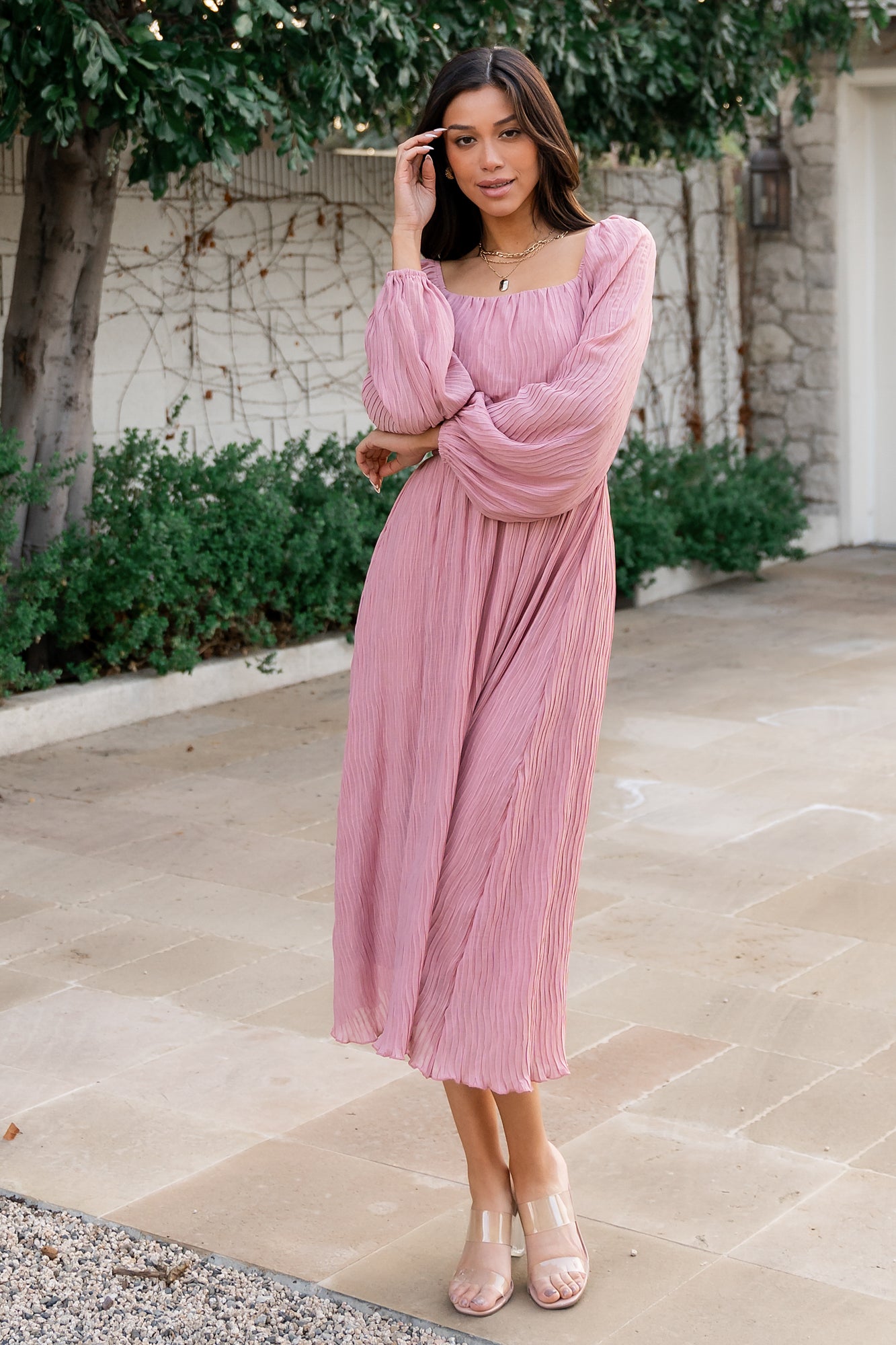 Rear and side view of Dalton pleated midi dress in blush showing asymmetrical lettuce ruffled hem and skirt length.
