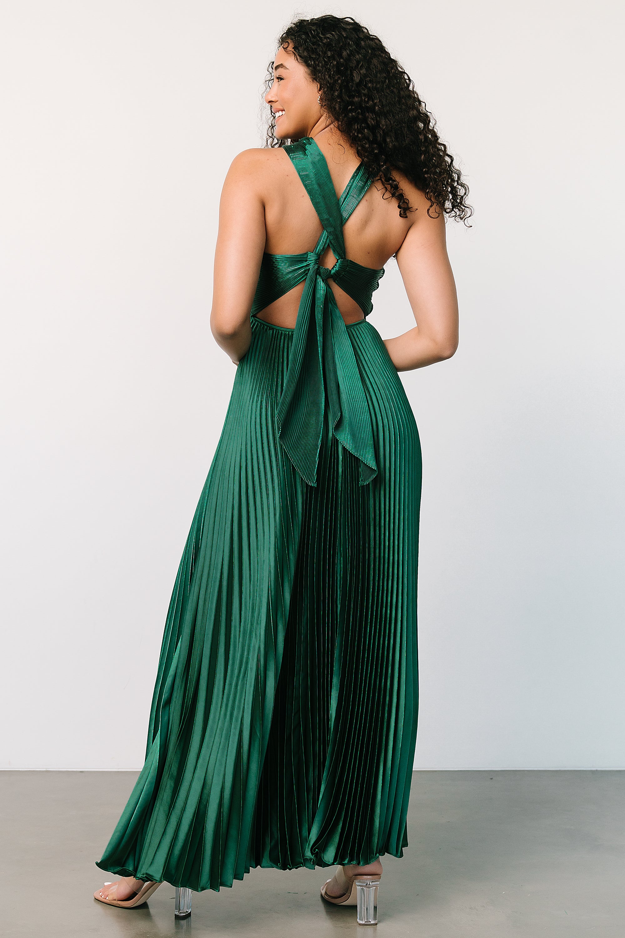 Side profile of the emerald pleated maxi highlighting the flowing skirt, waistline drape, and how the pleats catch light from the side.