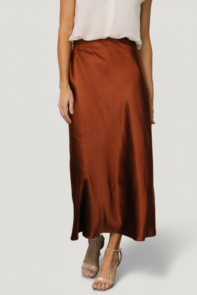 Front view of Celeste Satin Midi Skirt in spice rust on model; bias-cut silhouette, midi length, hidden waistband and side zipper detail, fabric sheen