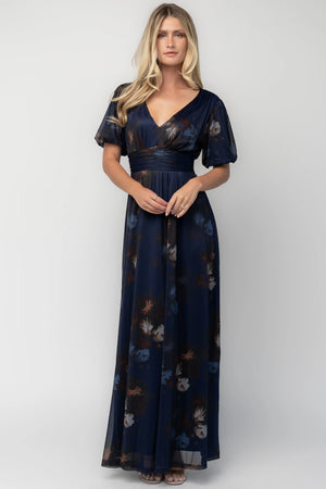 Model wearing the Whitney Mesh Maxi Dress in Navy, a navy floral mesh maxi dress with a deep V-neckline, short flutter sleeves, an empire waist, and a flowing A-line skirt with side pockets.