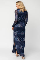 Model wearing a deep plum floral maxi dress with a fitted bodycon silhouette, sheer long sleeves, and a round neckline.