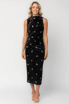 Model wearing a black velvet midi dress with a high neckline and fitted silhouette.