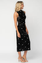 Model wearing a black velvet midi dress with a high neckline and fitted silhouette.