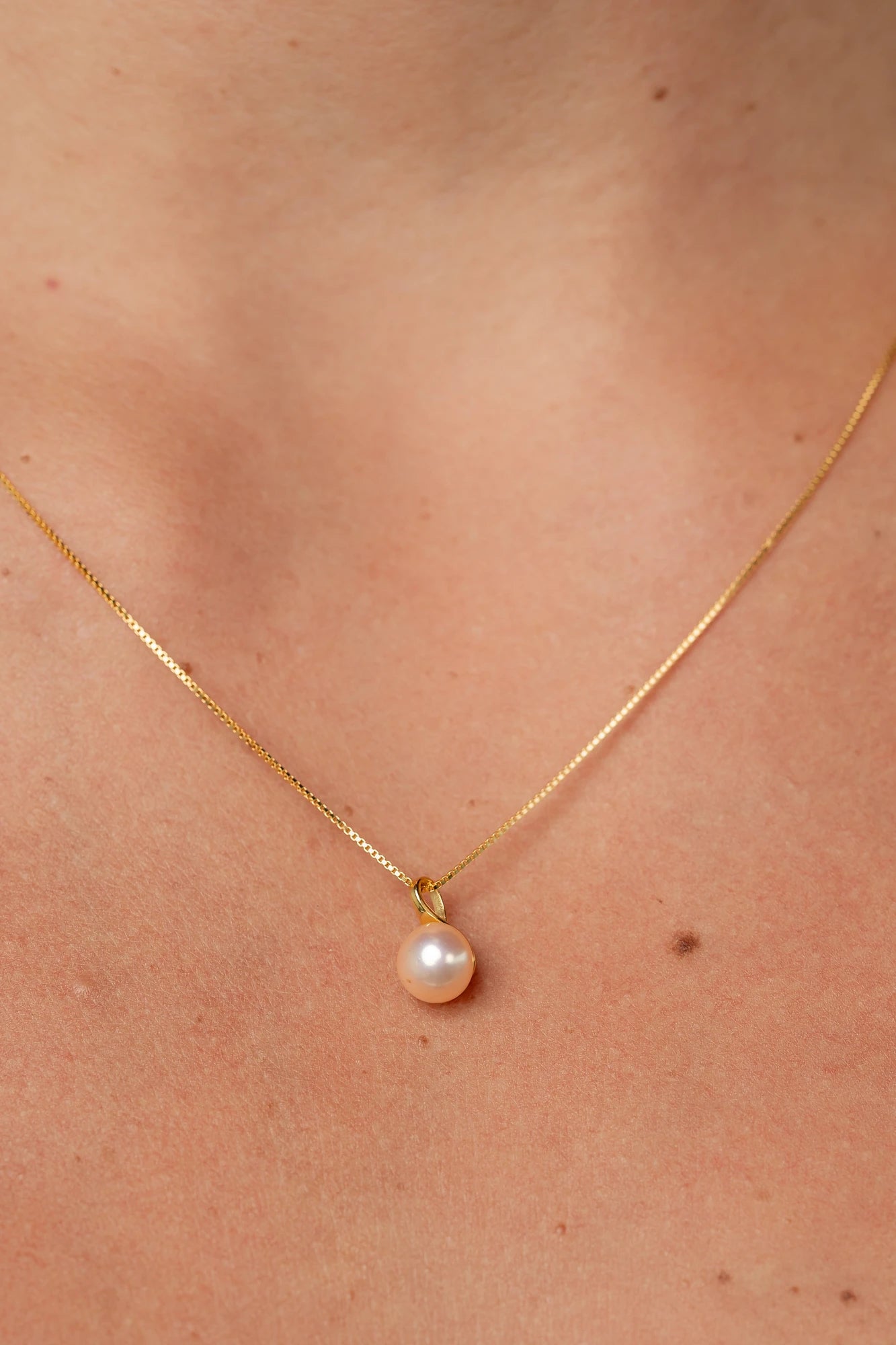 Gold necklace with a dainty chain and a single cultured freshwater pearl pendant.