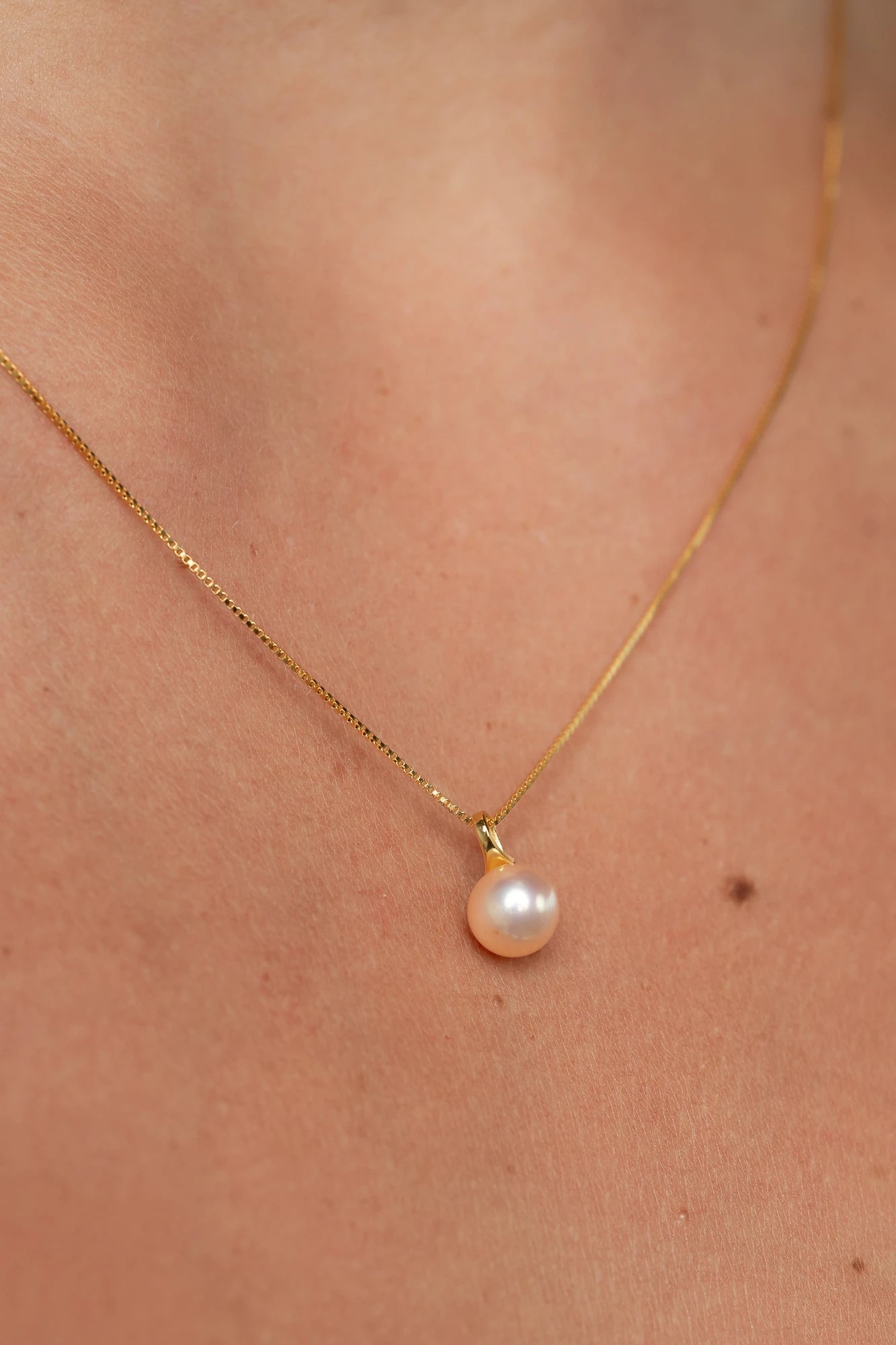 Gold necklace with a dainty chain and a single cultured freshwater pearl pendant.