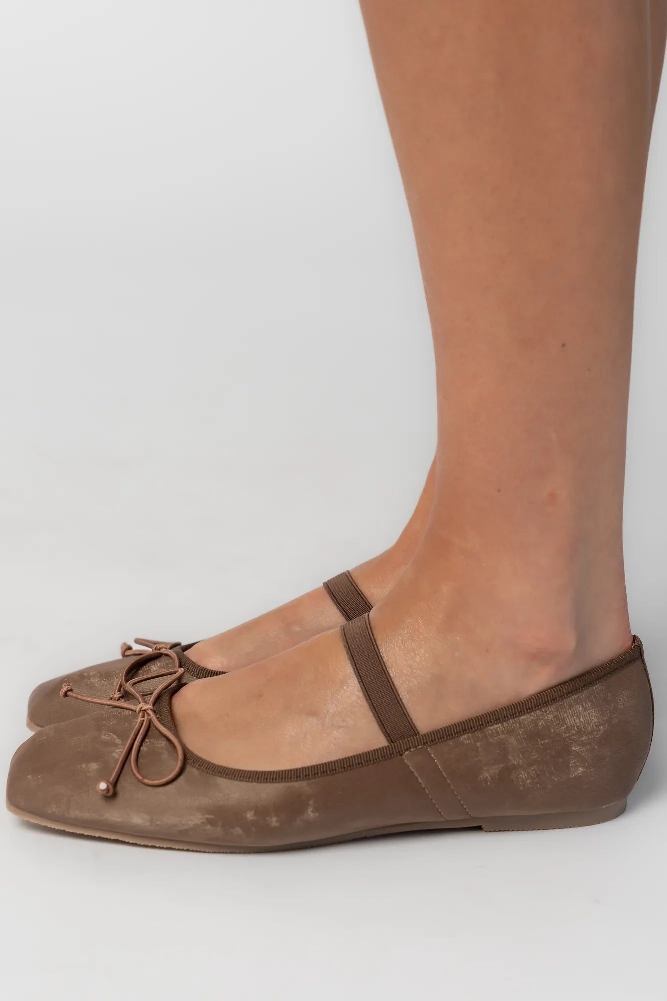 Pair of mocha velvet Mary Jane ballet flats featuring a square toe, delicate bow detail, and elastic strap across the foot. The classic flat silhouette offers a timeless, feminine look for everyday wear.