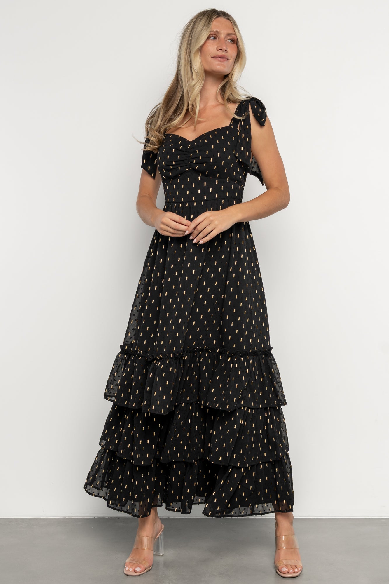 Full product view of Kassia Maxi Dress in black with gold accents, showing ruffle hem, empire waist, and overall silhouette.
