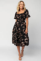 Model wearing a midi dress with a fully smocked bodice, square neckline, and short balloon sleeves.