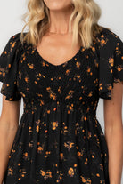 Model wearing a floral midi dress with a smocked bodice, wide V-neckline, and flutter sleeves.