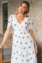Close-up of navy embroidered abstract flower detailing on off-white textured fabric, showing stitch and fabric texture.