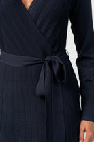 Cropped image of model wearing a navy midi dress with a surplice V-neckline, long sleeves, and a matching waist tie
