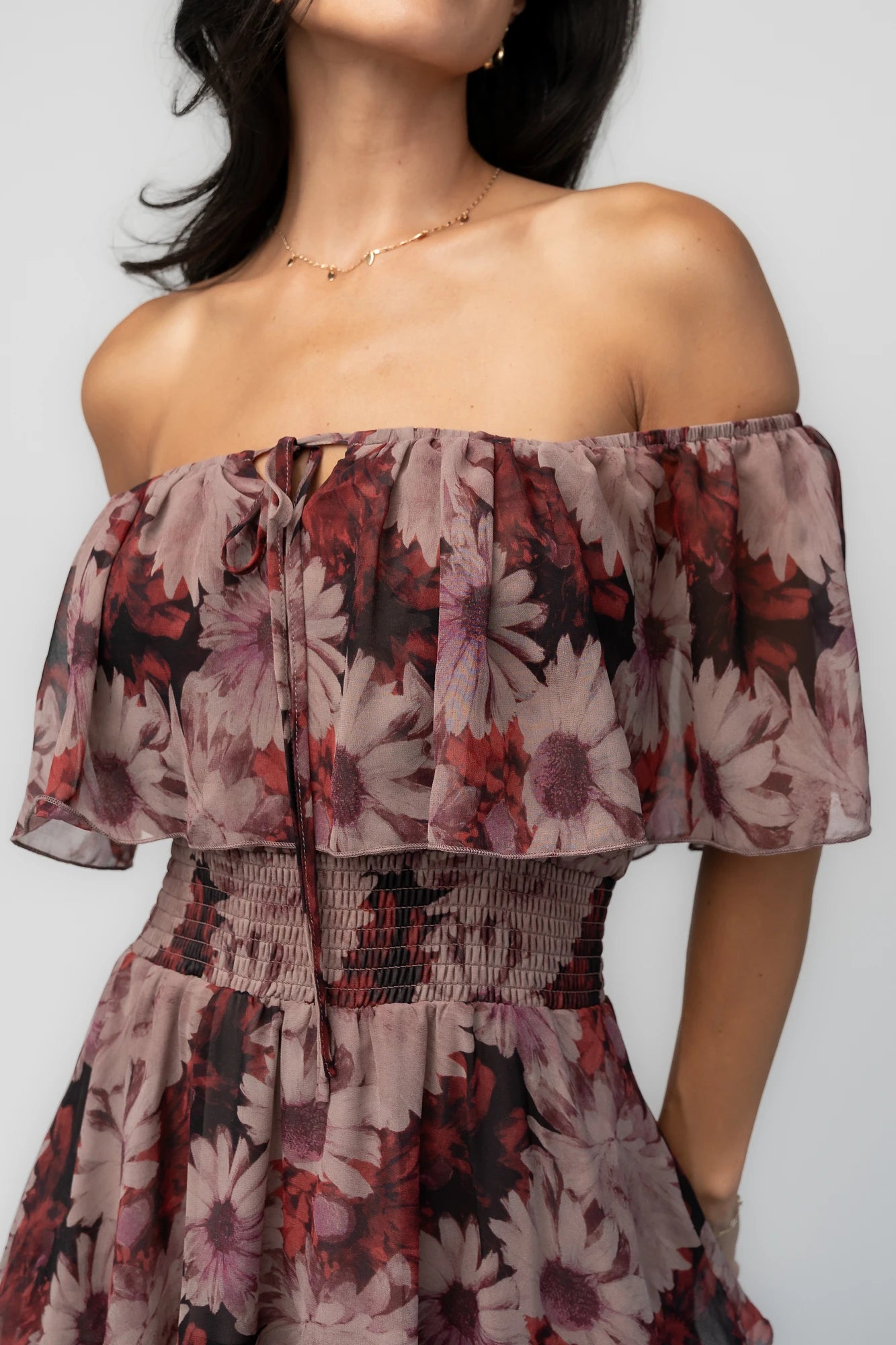 Model wearing the Carina Off-Shoulder Maxi in a soft multi floral print featuring a versatile neckline that can be worn on or off the shoulders, a ruffle overlay across the bust, a smocked waist, and a flowing four-tier maxi skirt.