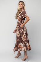 Model wearing the Blythe Midi Dress in Brown Floral featuring a collared neckline, functional button-front bodice, short rolled sleeves, and a removable waist tie.