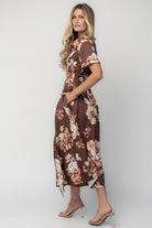 Model wearing the Blythe Midi Dress in Brown Floral featuring a collared neckline, functional button-front bodice, short rolled sleeves, and a removable waist tie.