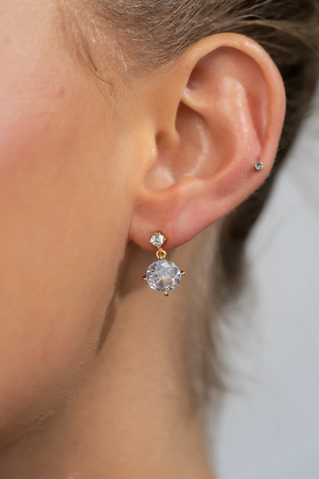 Model wearing gold-tone drop earrings featuring sparkling round zircon stones suspended from petite stud tops.